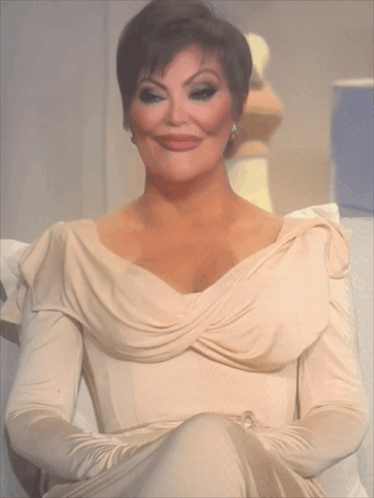 A Woman In A Beige Dress Is Sitting On A Couch With Her Arms Crossed GIF