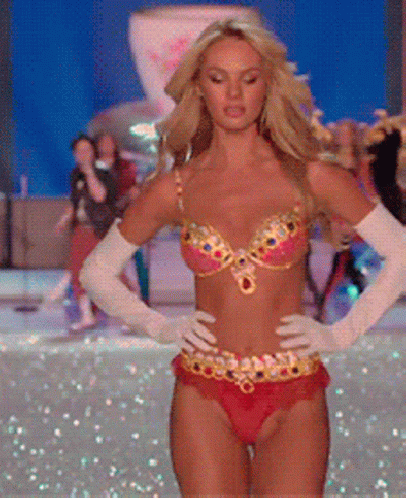 A Woman In A Bikini And White Gloves Is Walking On A Runway GIF