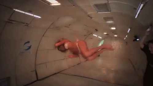 A Woman In A Bikini Is Floating In A Room With The Word Zero G On The Wall GIF