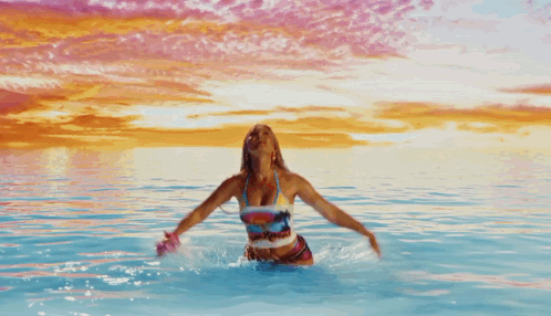 A Woman In A Bikini Is In The Water With Her Arms In The Air And A Shirt That Says Beach House GIF