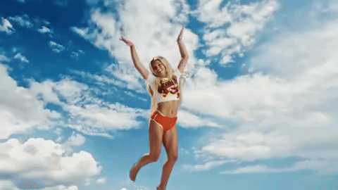 A Woman In A Bikini Is Jumping In The Air With Her Arms Outstretched GIF
