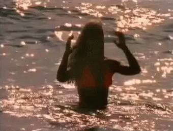 A Woman In A Bikini Is Standing In The Ocean At Sunset . GIF