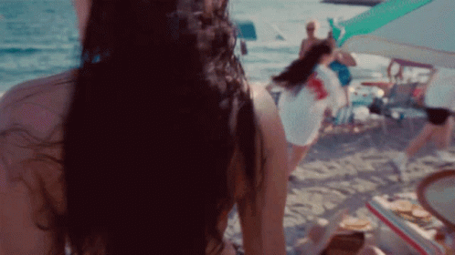 A Woman In A Bikini Is Standing On A Beach Looking At The Ocean GIF