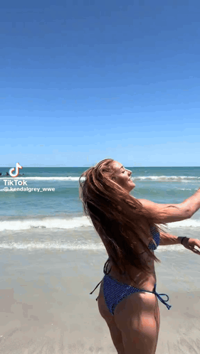 a woman in a bikini is standing on the beach with her arms outstretched .