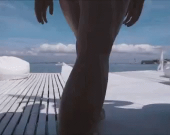 A Woman In A Bikini Is Walking On A Wooden Deck Towards The Ocean GIF