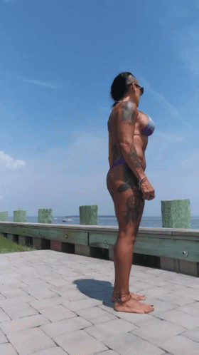 A Woman In A Bikini Stands On A Brick Walkway GIF
