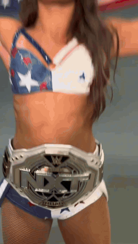 A Woman In A Bikini Top And Shorts Is Wearing A Nxt Championship Belt . GIF