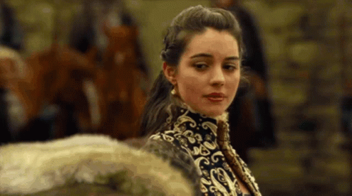 A Woman In A Black And Gold Dress Is Standing In Front Of A Group Of People . GIF