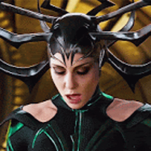 A Woman In A Black And Green Costume With Horns On Her Head Is Looking Down . GIF