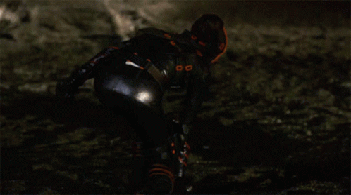 A Woman In A Black And Orange Outfit Is Kneeling Down GIF