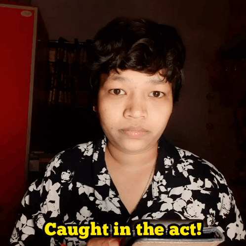A Woman In A Black And White Floral Shirt Is Holding A Cell Phone And Says Caught In The Act GIF