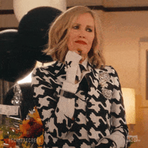 A Woman In A Black And White Houndstooth Suit Holds Her Hand To Her Chin . GIF