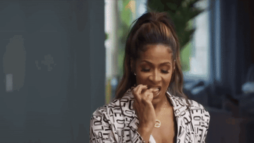 A Woman In A Black And White Jacket Is Eating A Piece Of Food . GIF