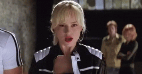 A Woman In A Black And White Jacket Is Standing In Front Of A Group Of People And Looking At The Camera . GIF