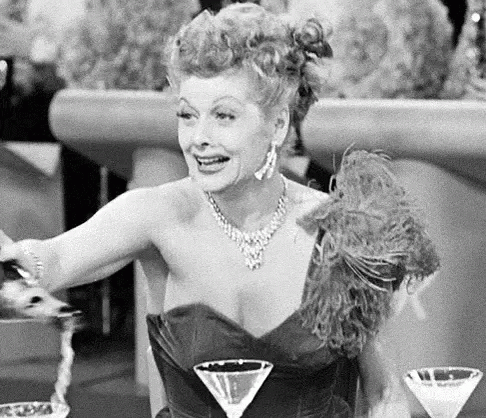 A Woman In A Black And White Photo Is Sitting At A Table With Two Martini Glasses . GIF