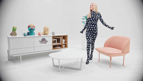 A Woman In A Black And White Polka Dot Outfit Stands In Front Of A Muppet Show Display GIF