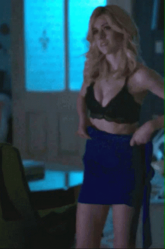 A Woman In A Black Bra And Blue Skirt Is Standing In A Living Room GIF