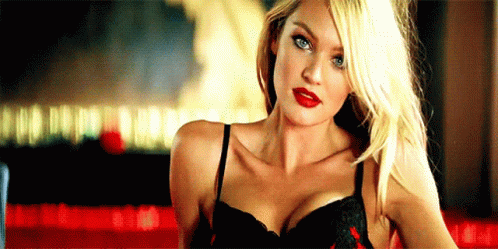 A Woman In A Black Bra And Red Lipstick Is Standing In Front Of A Red Table . GIF