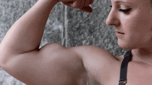 A Woman In A Black Bra Flexes Her Biceps GIF