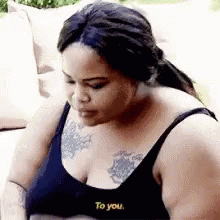 A Woman In A Black Bra Is Sitting On A Couch With A Tattoo On Her Chest . GIF