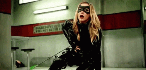 A Woman In A Black Catsuit Is Holding An Arrow . GIF