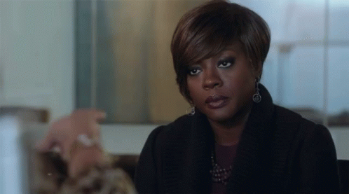 A Woman In A Black Coat And Earrings Is Sitting At A Table With A Man . GIF