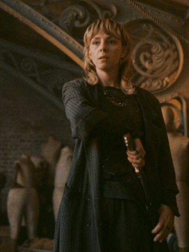 A Woman In A Black Coat Holds A Sword In Her Hand GIF