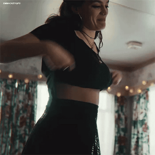 A Woman In A Black Crop Top And Black Skirt Is Standing In A Room GIF