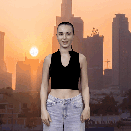 A Woman In A Black Crop Top And Jeans Stands In Front Of A City Skyline GIF