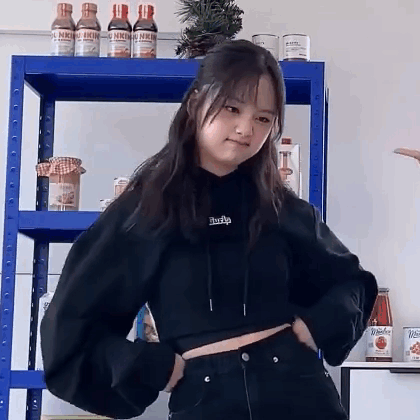 A Woman In A Black Crop Top Is Standing In Front Of A Blue Shelf . GIF