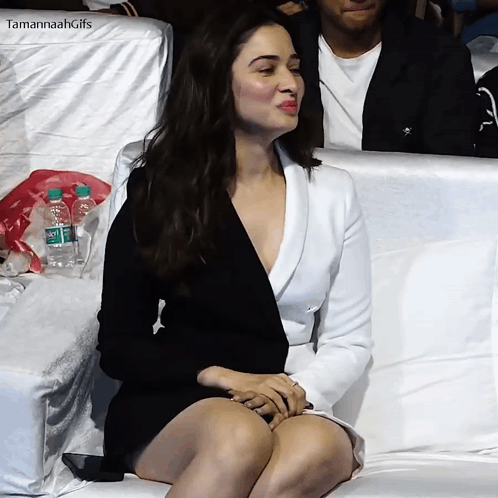 A Woman In A Black Dress And White Jacket Is Sitting On A White Couch GIF