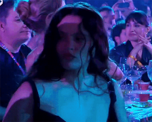 A Woman In A Black Dress Is Dancing In A Crowd Of People GIF