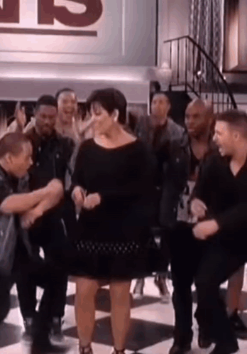 A Woman In A Black Dress Is Dancing In Front Of A Group Of People . GIF