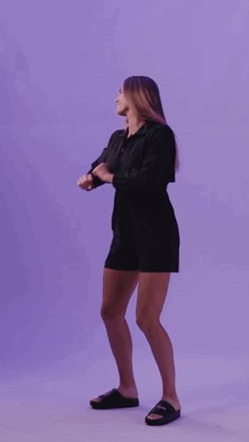 a woman in a black dress is dancing in front of a purple wall