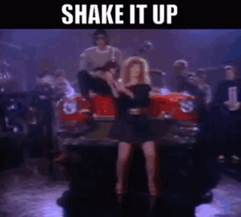 A Woman In A Black Dress Is Dancing In Front Of A Red Car With The Words Shake It Up Above Her GIF