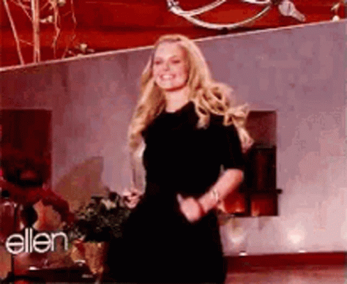 A Woman In A Black Dress Is Dancing On A Stage In Front Of A Wall With The Word Ellen On It . GIF