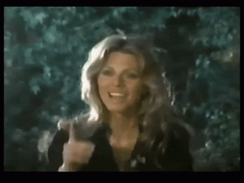 A Woman In A Black Dress Is Giving The Middle Finger While Standing In Front Of Trees . GIF