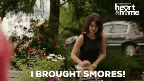 A Woman In A Black Dress Is Holding A Basket And Says " I Brought Smores " GIF