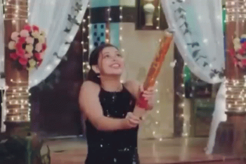 A Woman In A Black Dress Is Holding A Bat In Her Hand And Throwing It In The Air . GIF