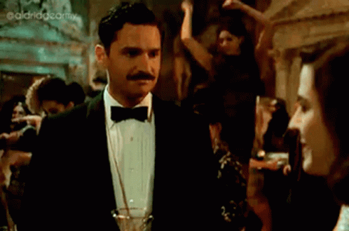 A Woman In A Black Dress Is Holding A Glass Of Champagne GIF
