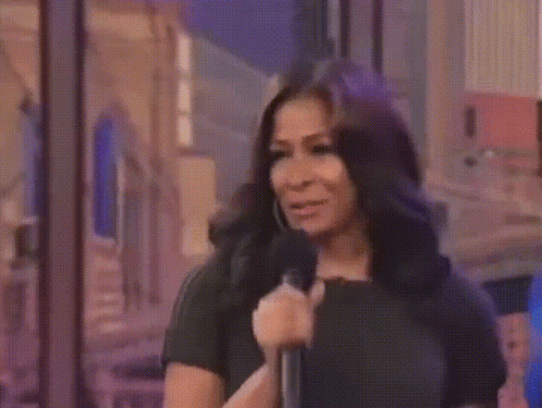 A Woman In A Black Dress Is Holding A Microphone GIF
