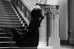 A Woman In A Black Dress Is Kneeling Down On The Stairs In A Black And White Photo . GIF