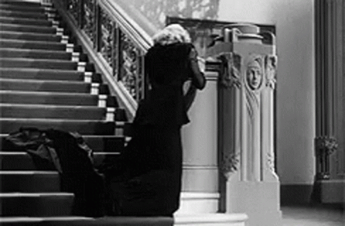 A Woman In A Black Dress Is Kneeling Down On The Stairs In A Black And White Photo . GIF