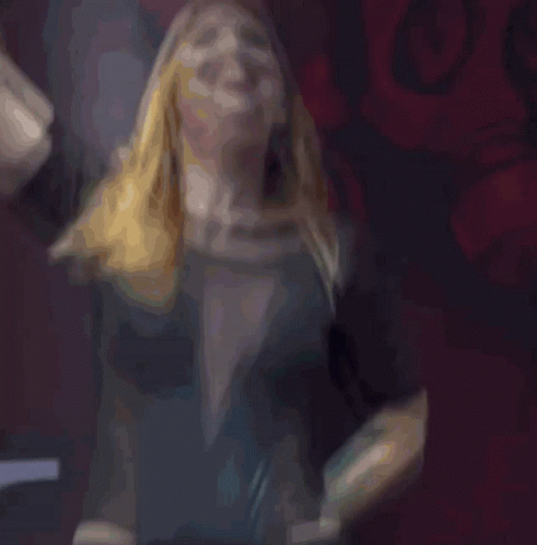 A Woman In A Black Dress Is Screaming With Her Hand In The Air GIF