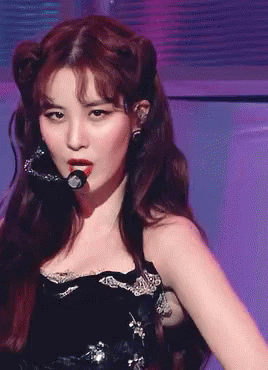 A Woman In A Black Dress Is Singing Into A Microphone On A Stage GIF