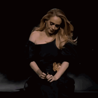 A Woman In A Black Dress Is Sitting Down GIF