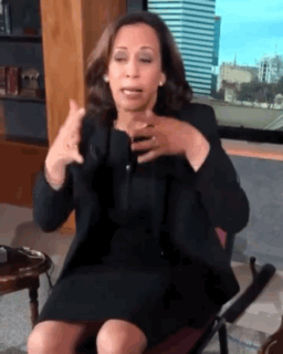 A Woman In A Black Dress Is Sitting In A Chair Making A Gesture GIF