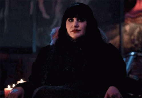 a woman in a black dress is sitting in a chair with candles in the background .