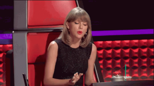 A Woman In A Black Dress Is Sitting In A Red Chair With A Cup Of Coffee GIF