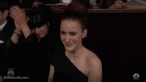 a woman in a black dress is sitting in a theatre applauding a man .